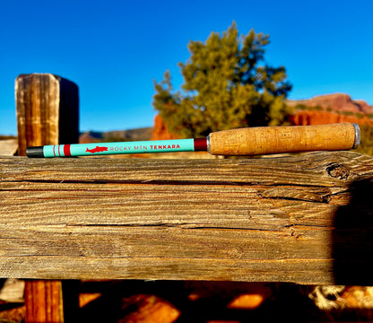 A Tenkara fishing rod with a cork handle, laid on a wooden surface with a scenic background of red rock formations.