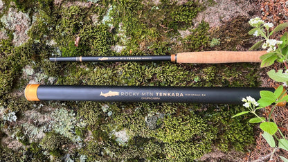 A two-piece Rocky MTN Tenkara fishing rod placed on a mossy surface, with the brand logo visible on the cork handle.